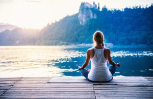 Yoga lotus. Young woman doing yoga by the lake, sitting in lotus.